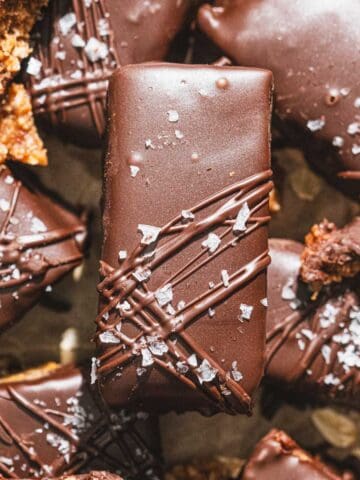 Chocolate almond bars with a drizzle of chocolate and flaky sea salt on parchment paper.