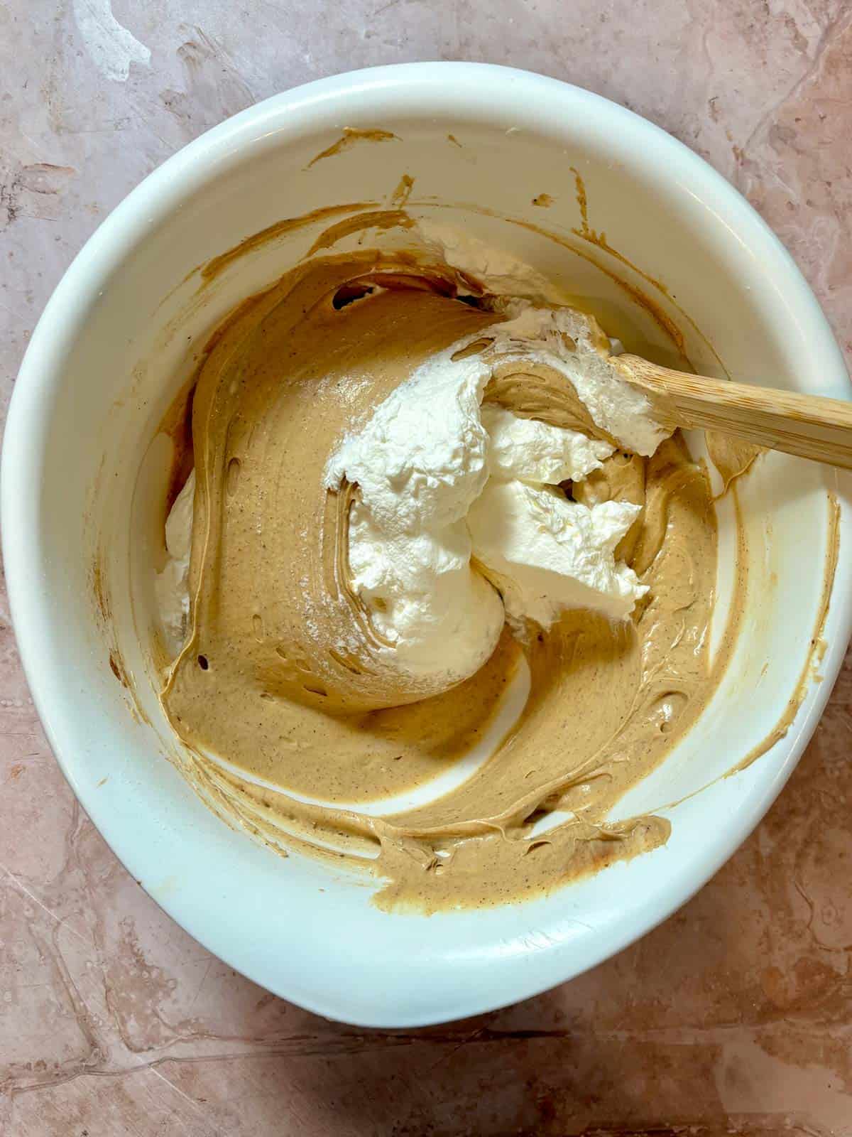 Gingerbread cream cheese mixture being folded with whipped cream in a bowl.
