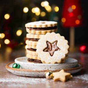 A stack of espresso shortbread cookies on 2 plates with Christmas lights in the background.