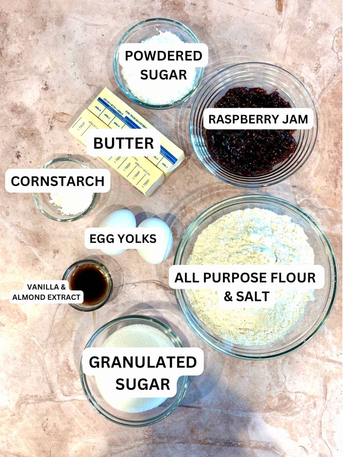 Ingredients out on the counter, sugar, butter, raspberry jam, almond extract, eggs, and powdered sugar.