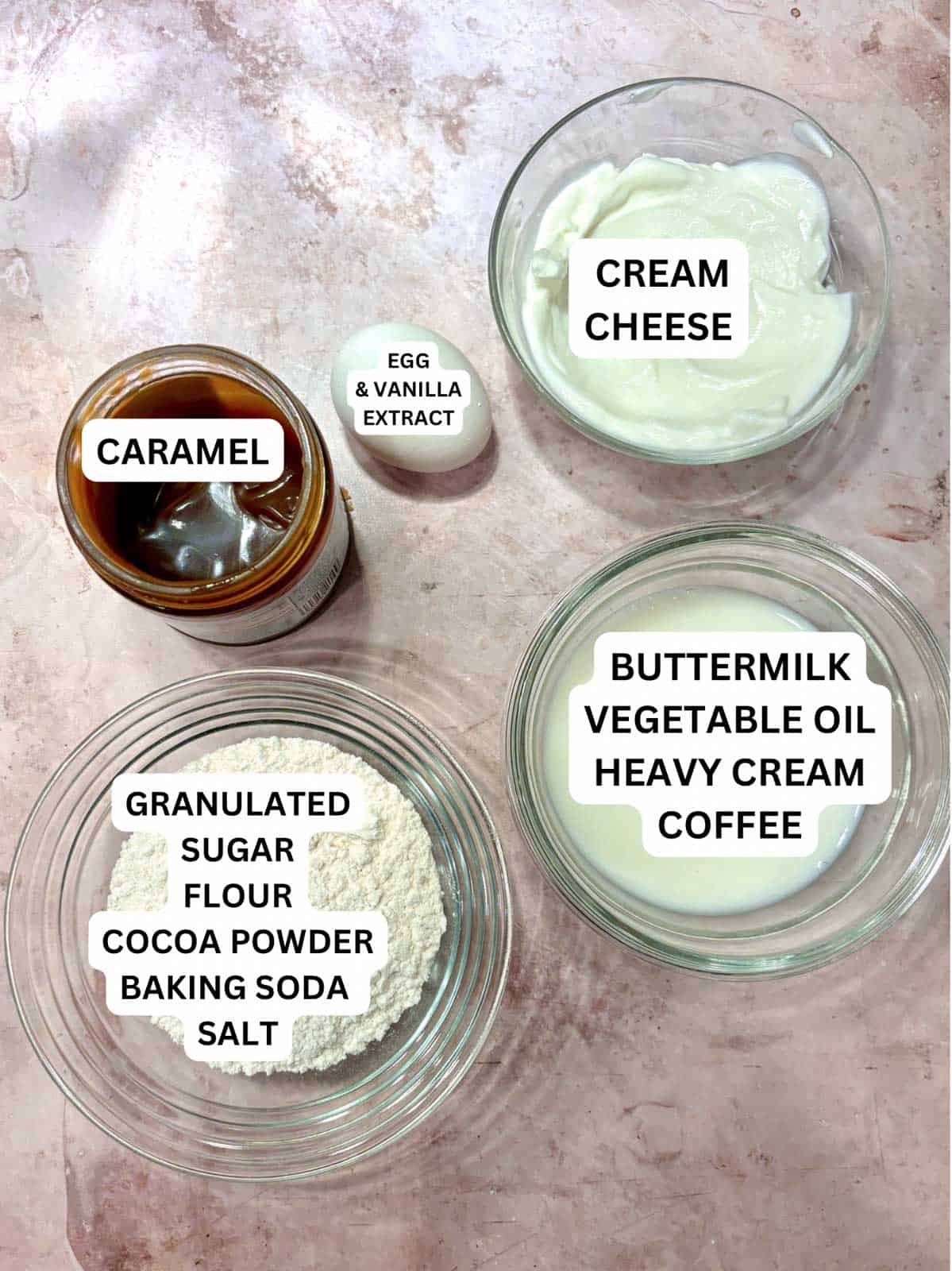 Ingredients consisting of cream cheese, cocoa powder, flour, sugar, baking soda, buttermilk, oil, caramel, and egg on the counter.
