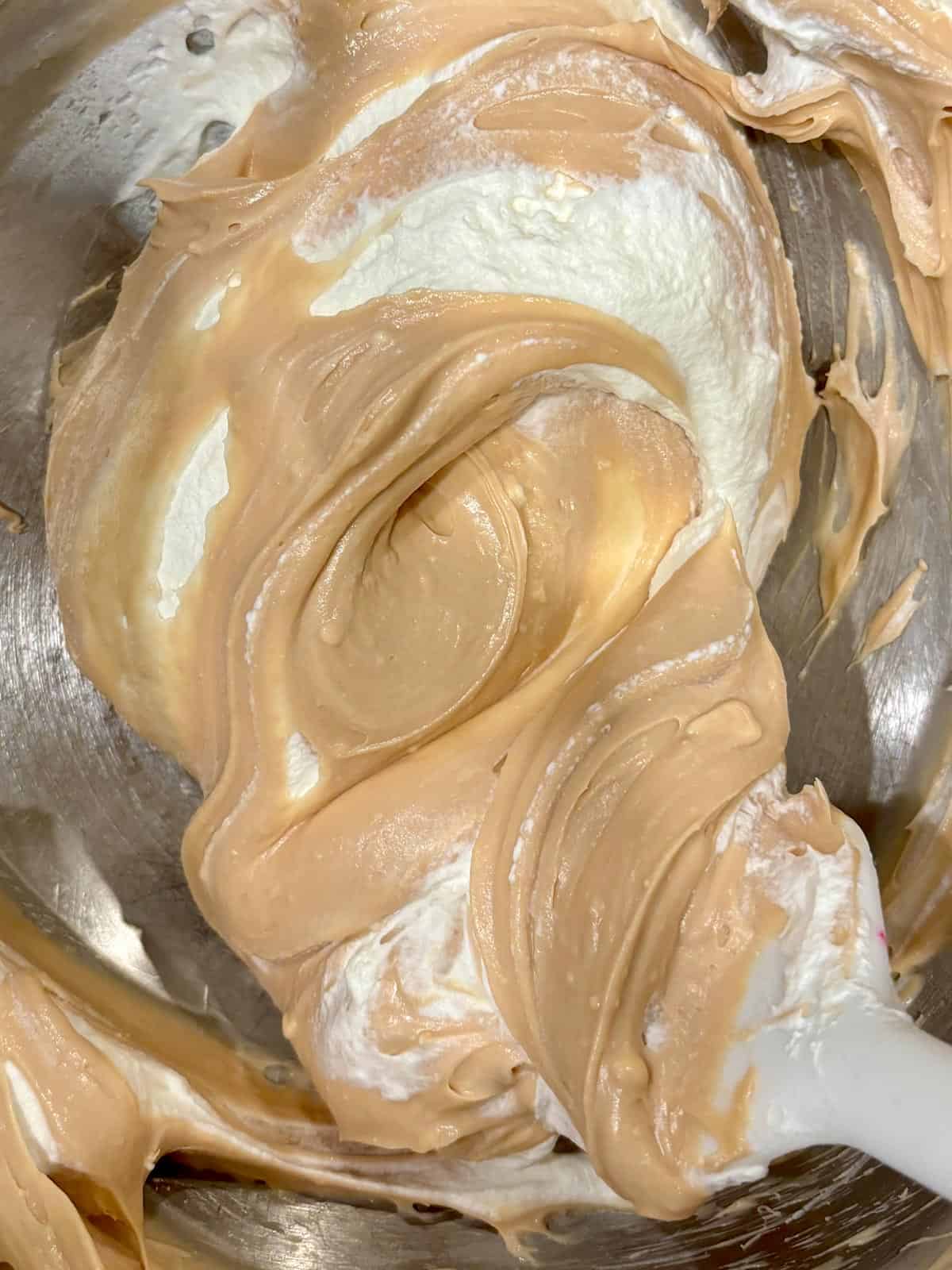 Caramel and cream cheese in a mixing bowl with whipped cream being folded in.