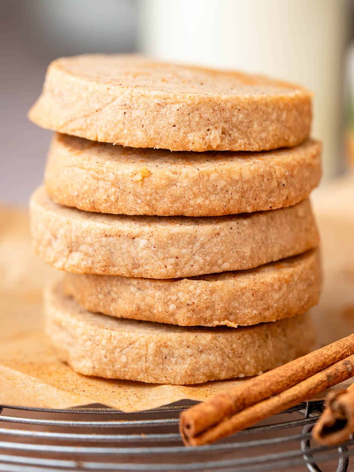 A stack of shortbread cookies on a wire rack with cinnamon sticks.