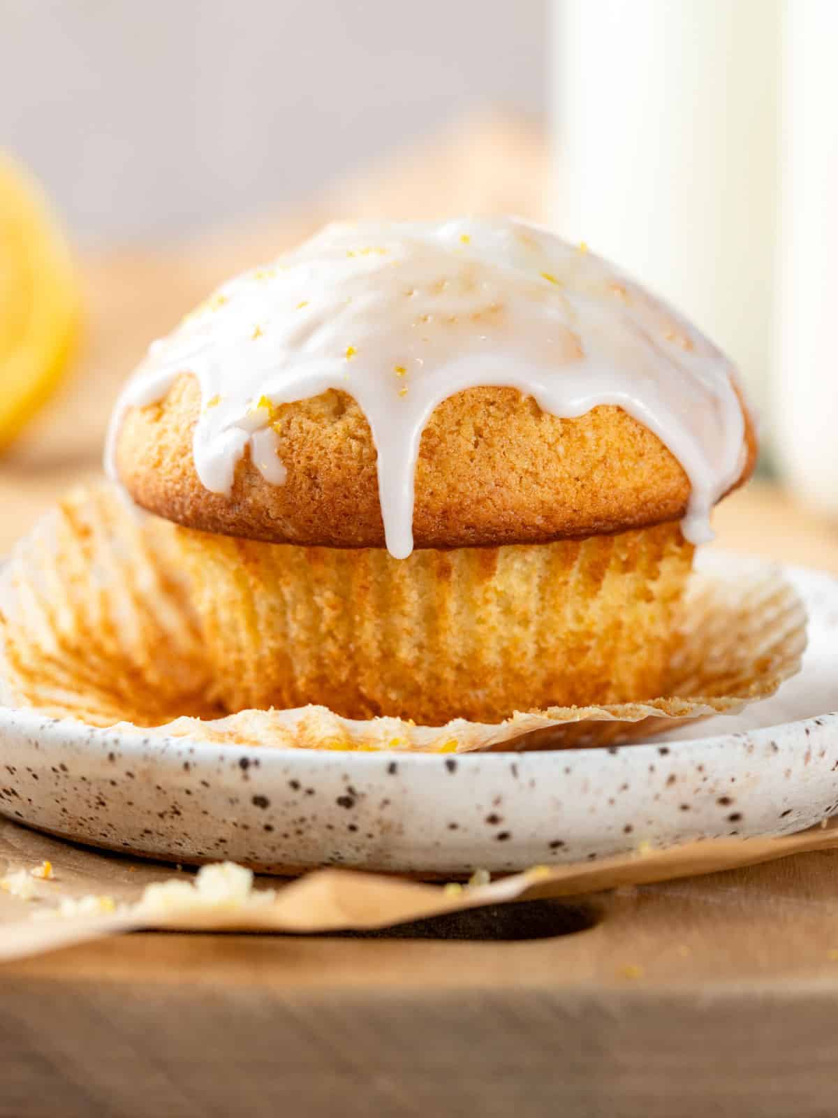 A bakery style muffin on a plate with lemon glaze dripping off the top.