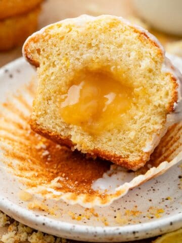 One lemon curd muffin cut in half with the lemon curd showing on a plate.