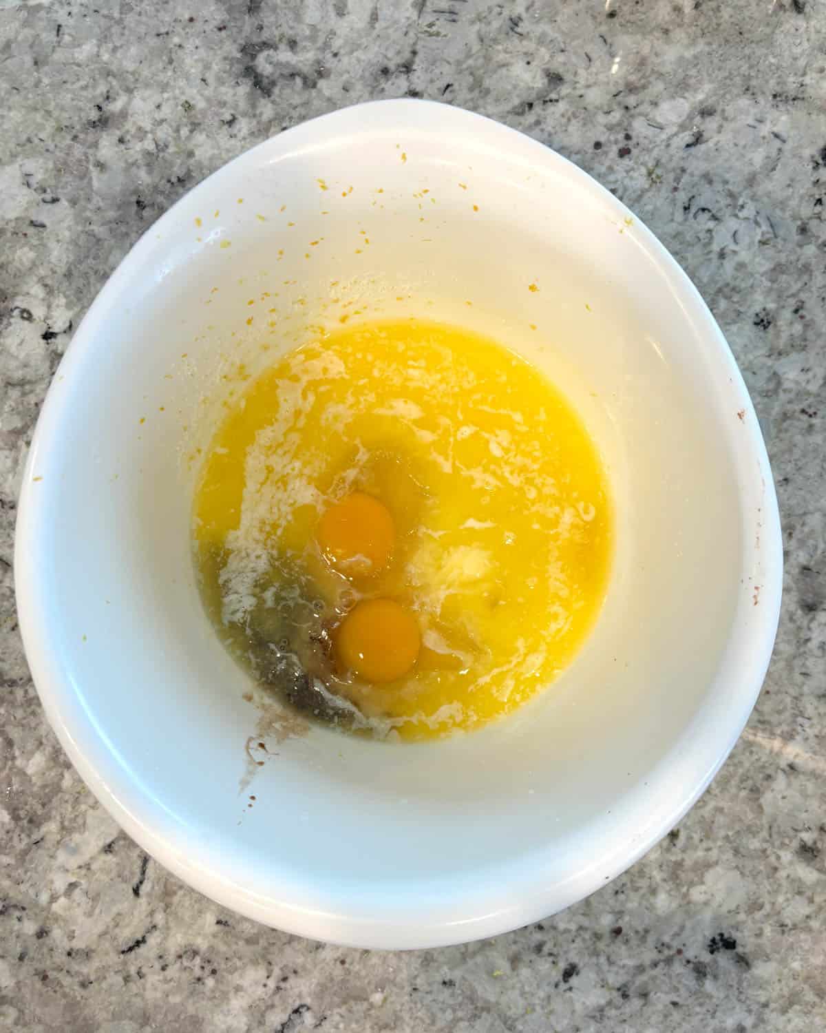 A white bowl full of eggs, sugar, melted butter, vegetable oil, and milk reading to be mixed.