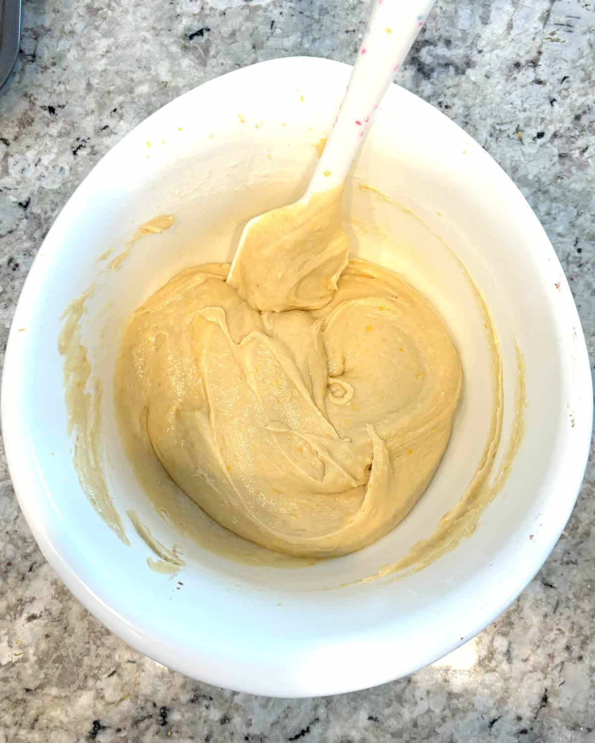 Lemon muffin batter in a white bowl with a spatula.