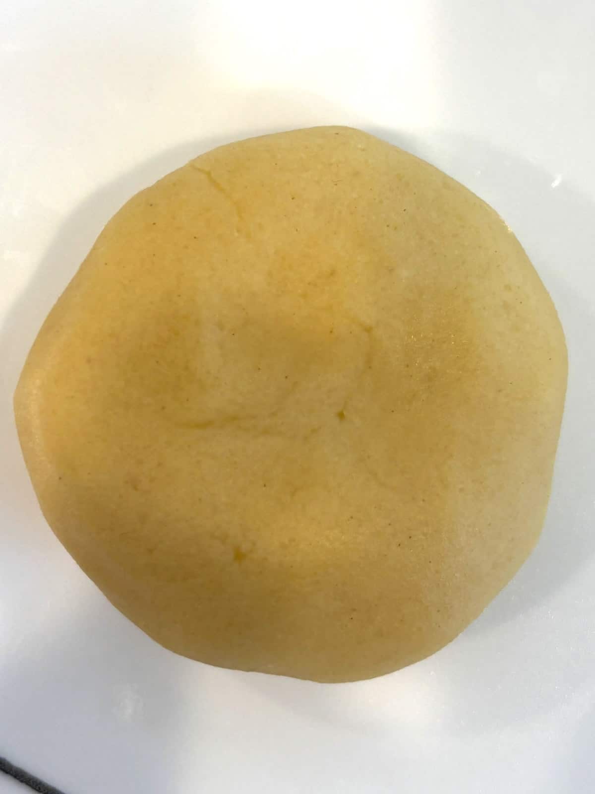 A ball of almond cookie dough slightly flattened before making a heart indent.