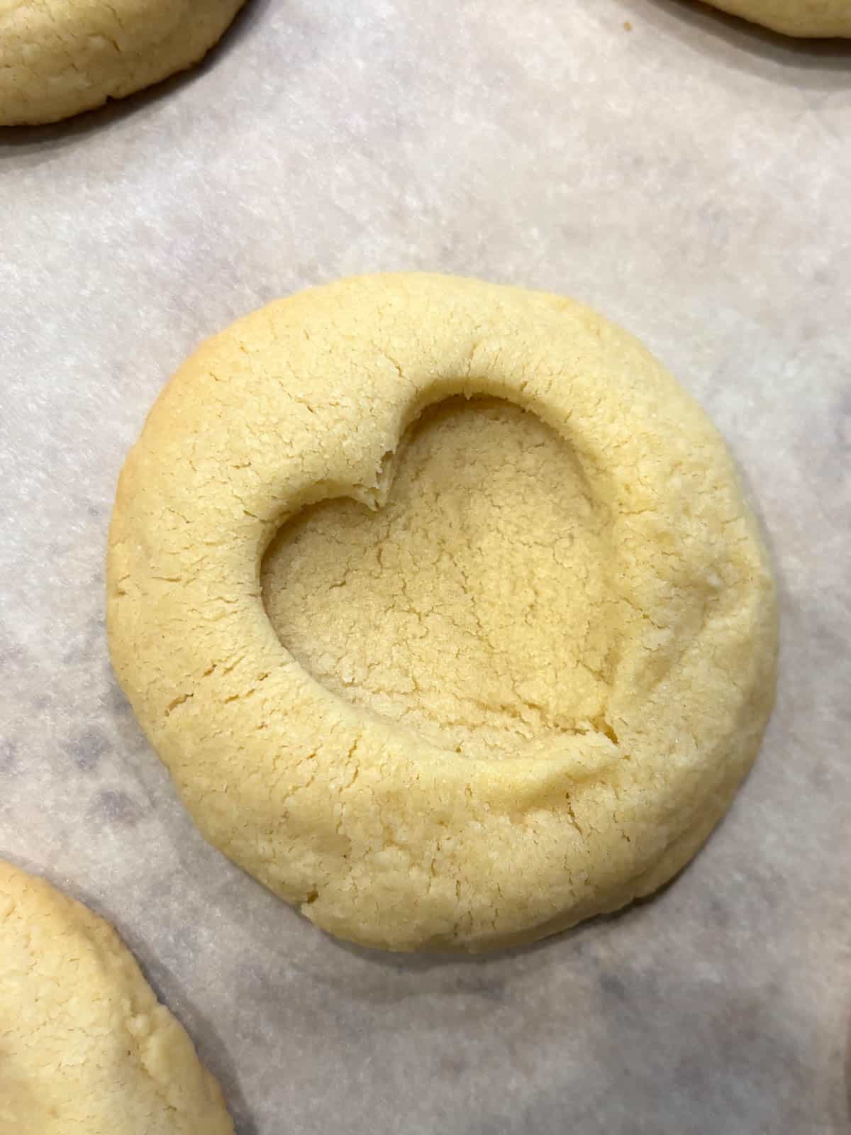 An almond shortbread cookie with an indent in the shape of a heart on a piece of parchment paper.