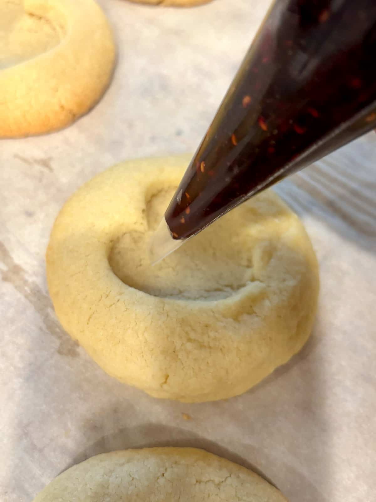 Raspberry jam being piped into an almond thumbprint cookie.