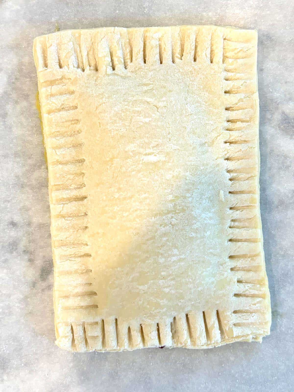 An assembled pop tart with crimped edges on a piece of parchment paper.