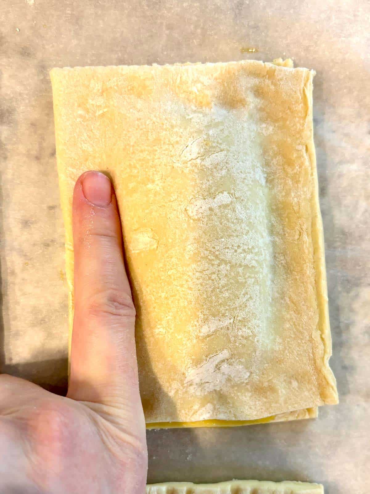 A piece of puff pastry being put on top of the blueberry jam to create a pop tart.