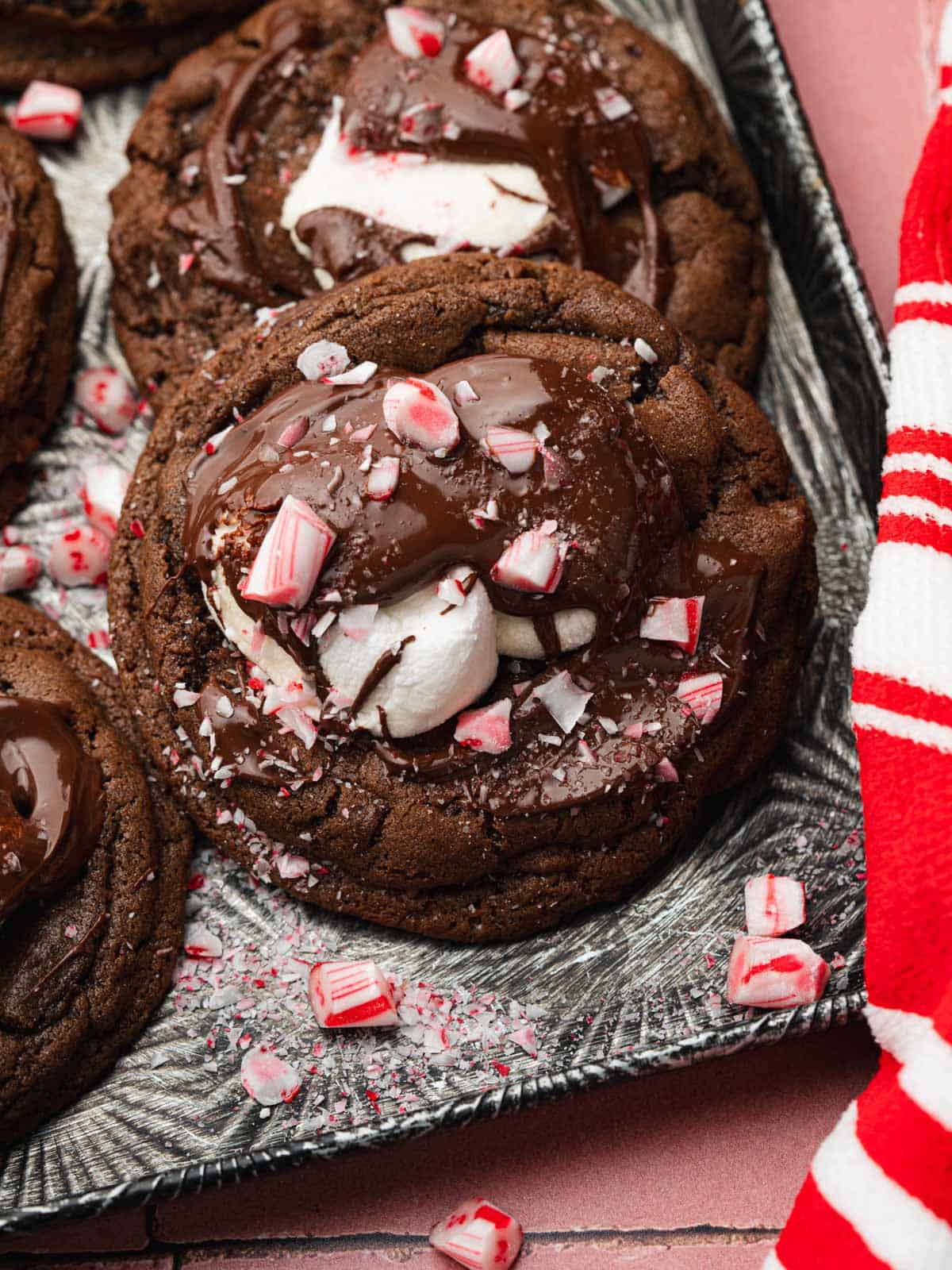 Chocolate cookies stacked on a cookie sheet with marshmallows and peppermint candies.