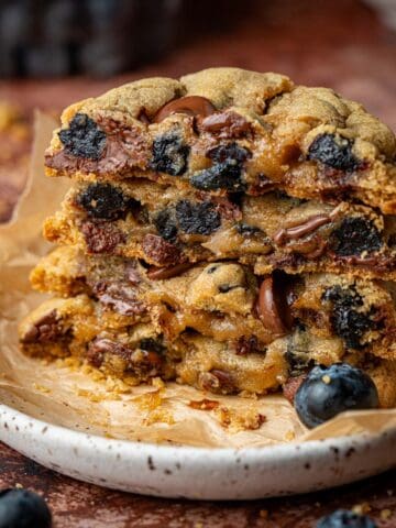 Blueberry chocolate cookies stacked on a plate with blueberries around.