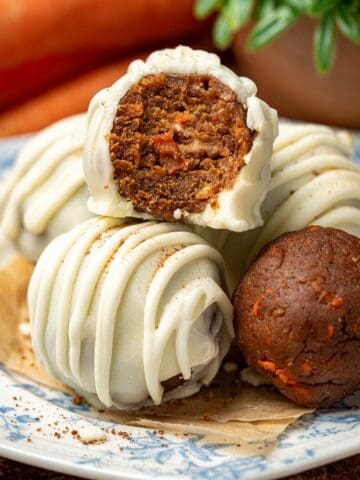 Carrot cake truffles on a plate with carrots in the background.