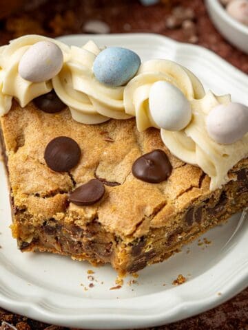 Easter cookie cake on a plate with cream cheese frosting and Cadbury mini eggs on top.