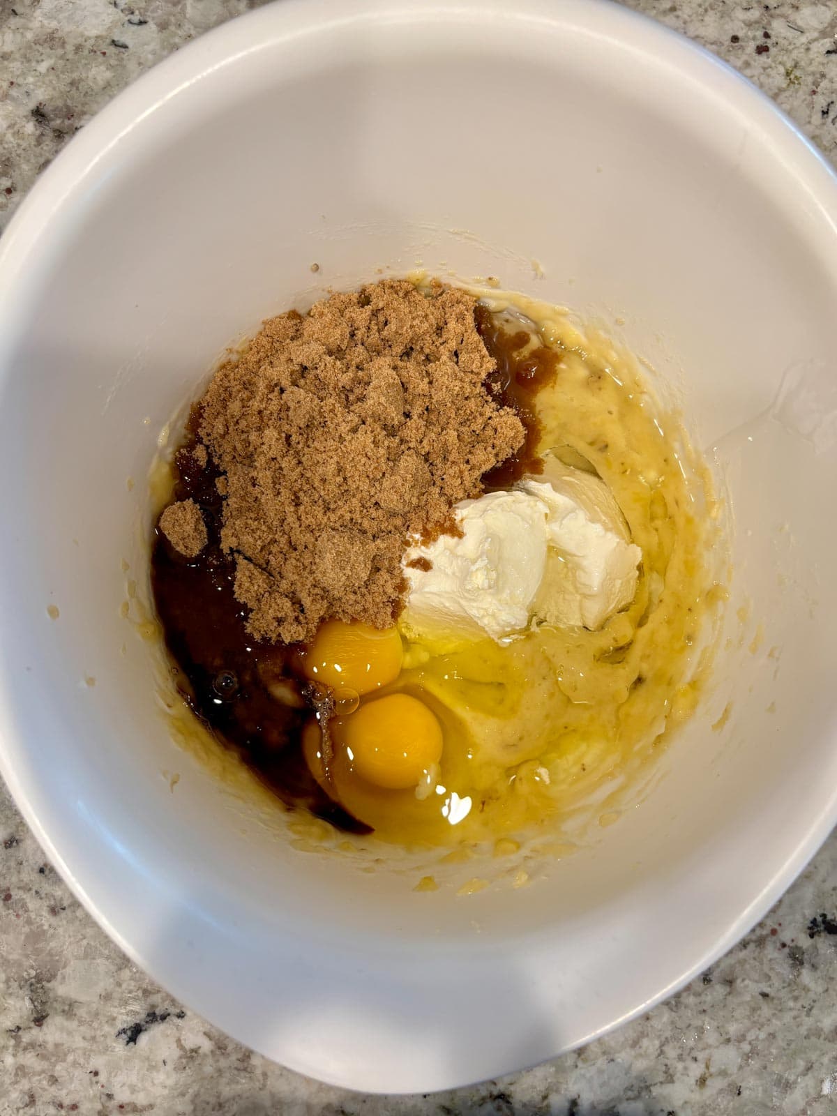 Bananas, sugar, eggs, oil, and sour cream in a bowl to be mixed.