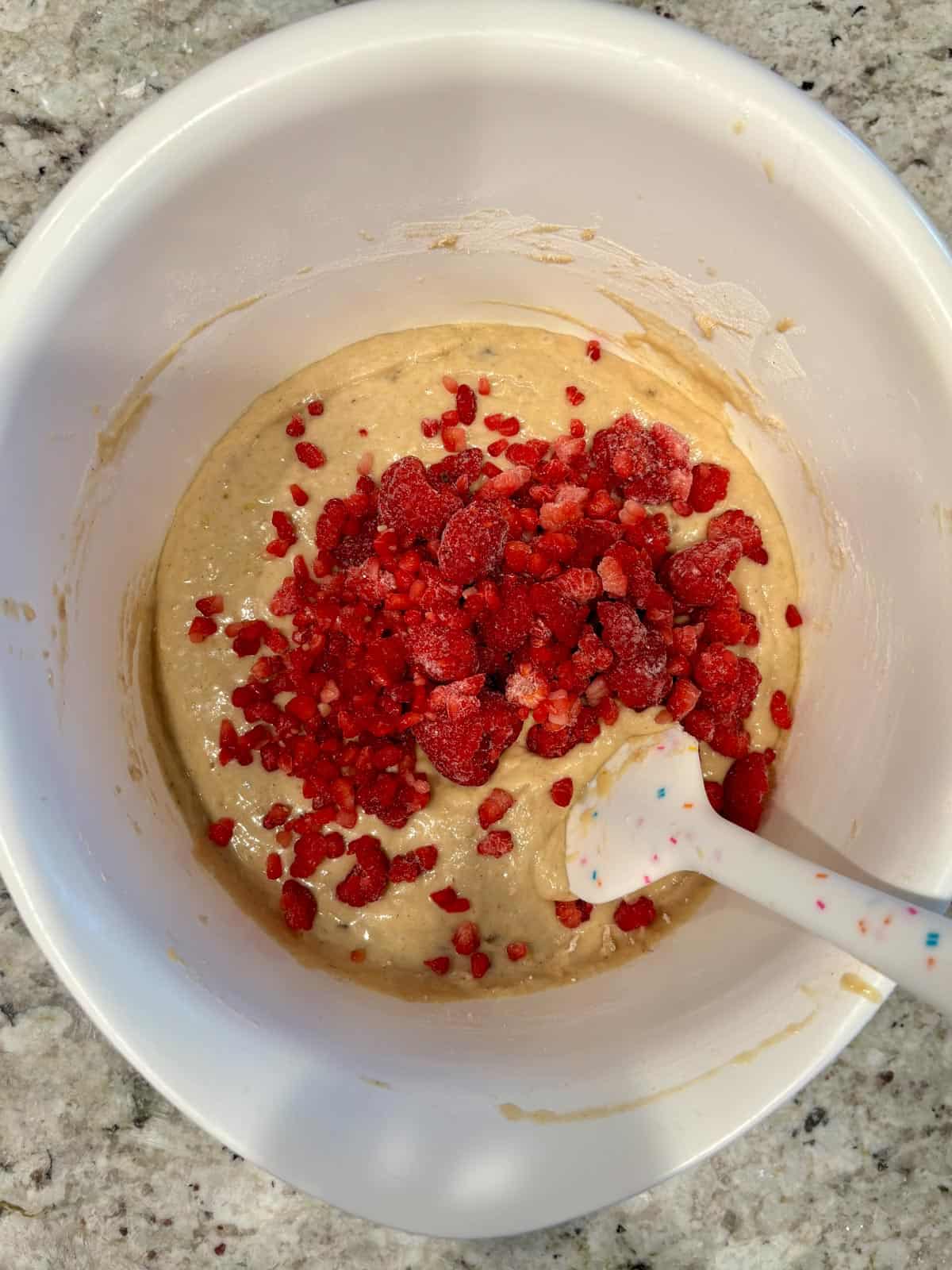 Raspberries being folded into the muffin batter in a bowl.