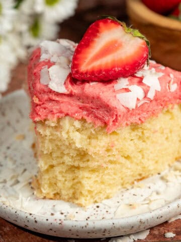 Coconut and strawberry cake on a plate with shredded coconut and a fresh strawberry on top.