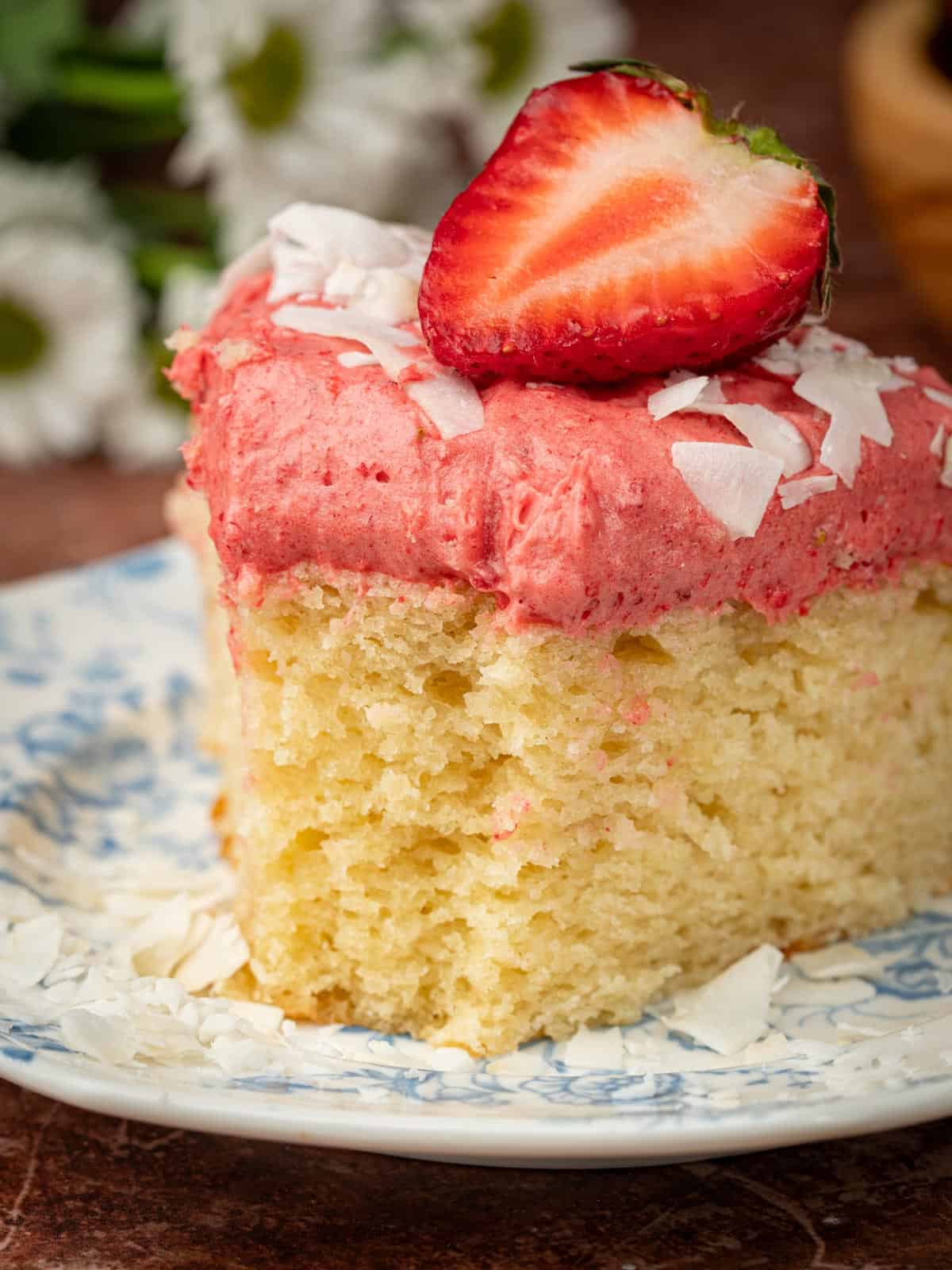 Coconut strawberry cake on a plate with shredded coconut and a fresh berry.