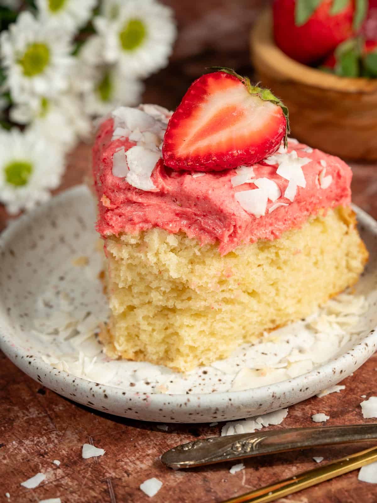 Strawberry coconut cake on a plate with shredded coconut and flowers around it.