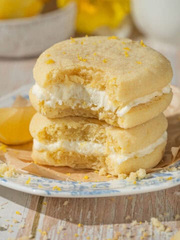 Lemon cookie sandwiches stacked on top of one another with lemons.
