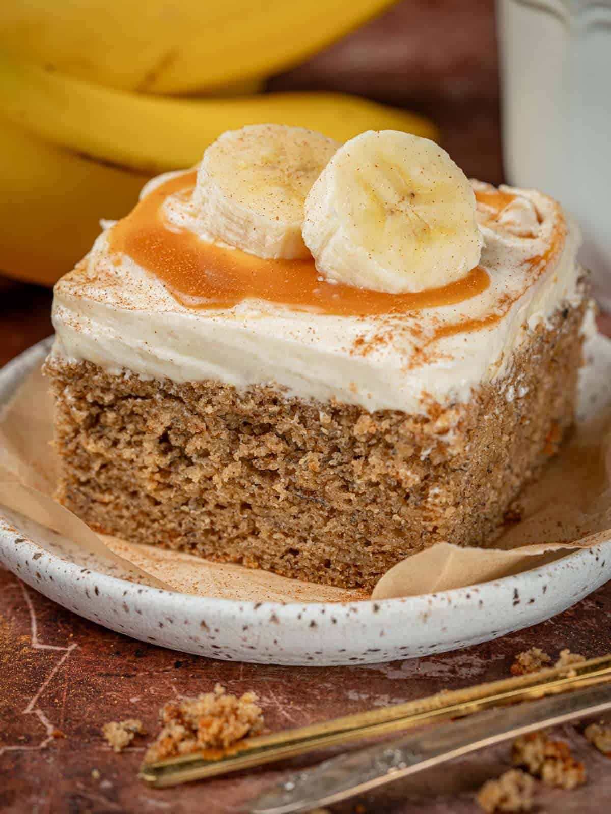 Spice banana cake on a plate with cream cheese frosting and salted caramel.
