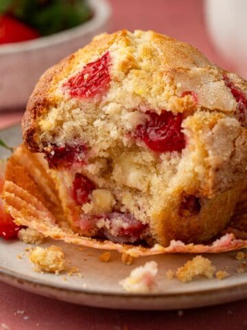 Strawberry and white chocolate muffin on a plate with a muffin liner and berries.