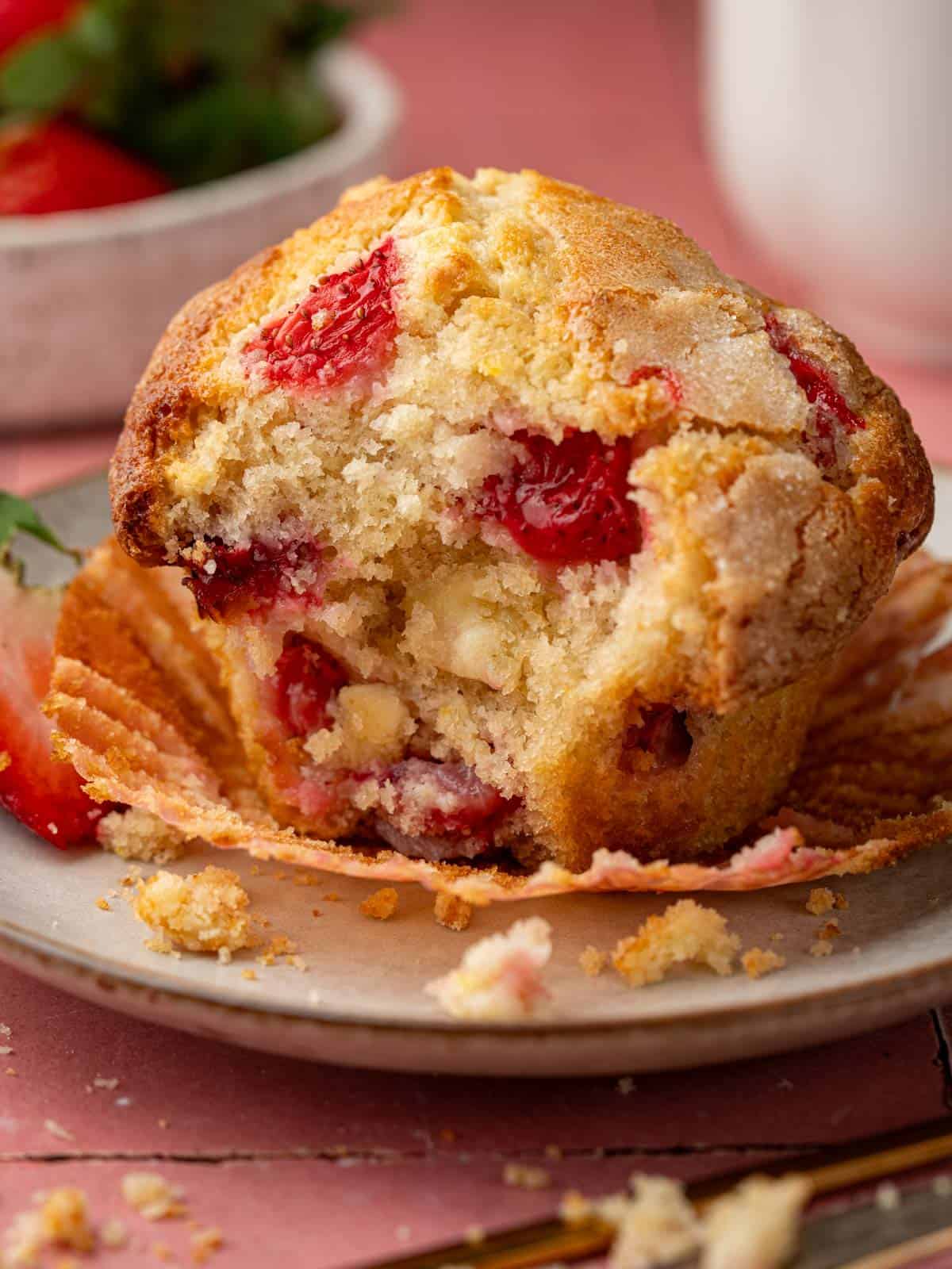 Strawberry white chocolate muffin on a plate with strawberries in the background.