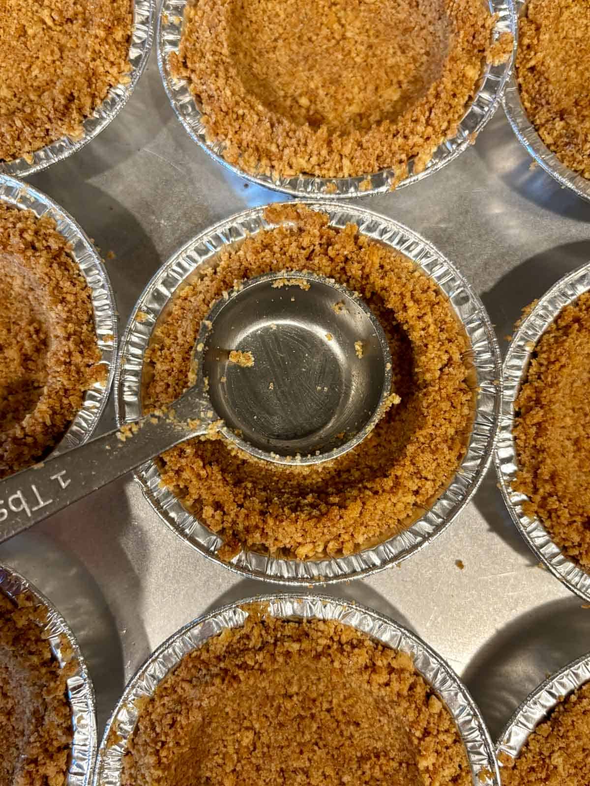 Mini graham cracker crusts being packed into the mini pie tins.