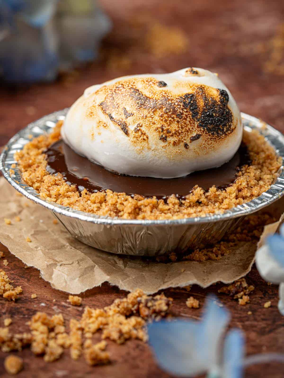 Mini s'mores pies on the counter with torched marshmallow and graham cracker crumbs.