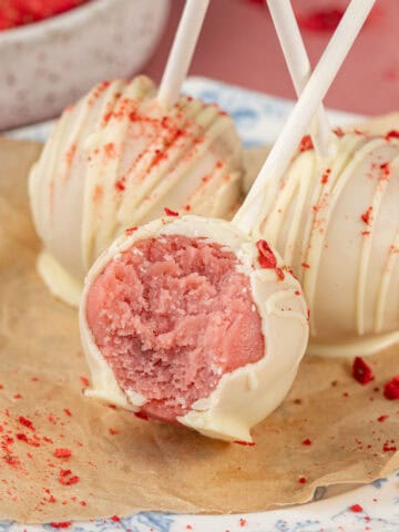 Strawberry cake pops on a plate with a bite taken out.