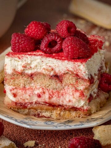 Almond tiramisu on a plate with ladyfingers around and raspberries.
