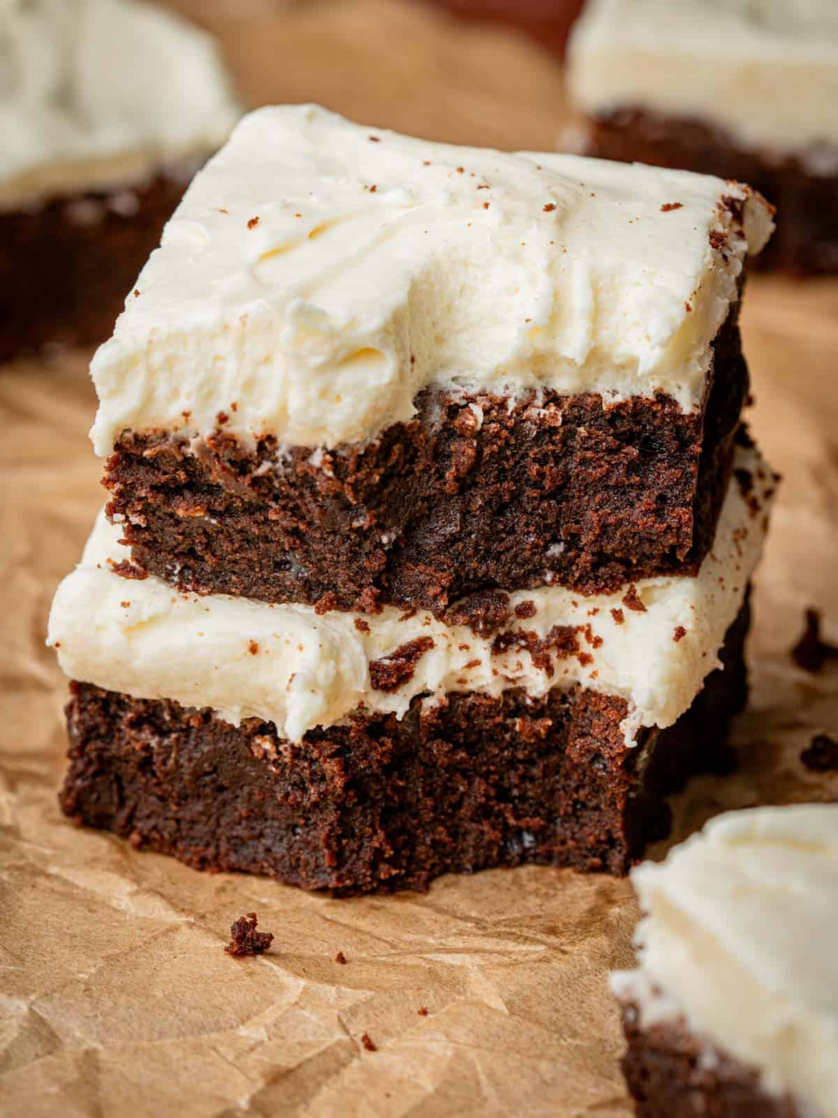 Brownies stacked with cream cheese frosting on top with parchment paper.