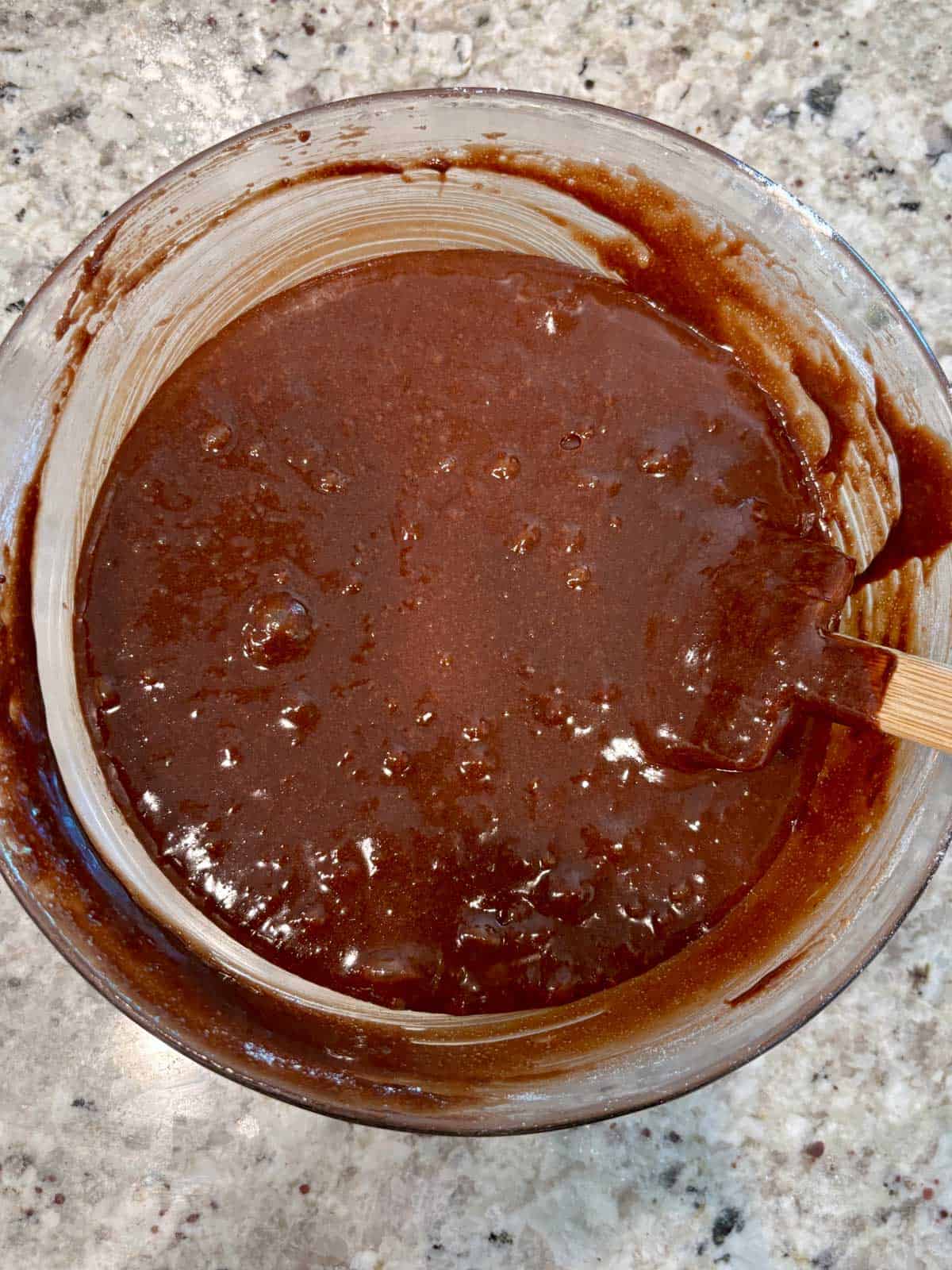 Chocolate brownie batter in a bowl with a spatula being mixed.