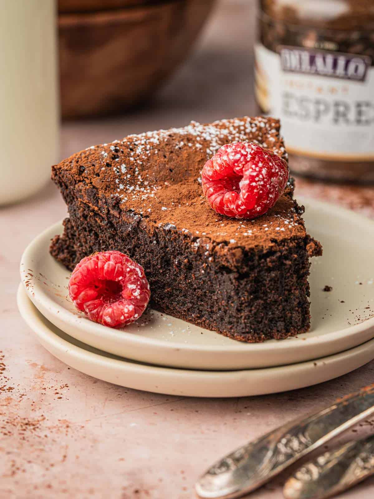 A slice of torte with espresso powder in the background and raspberries.