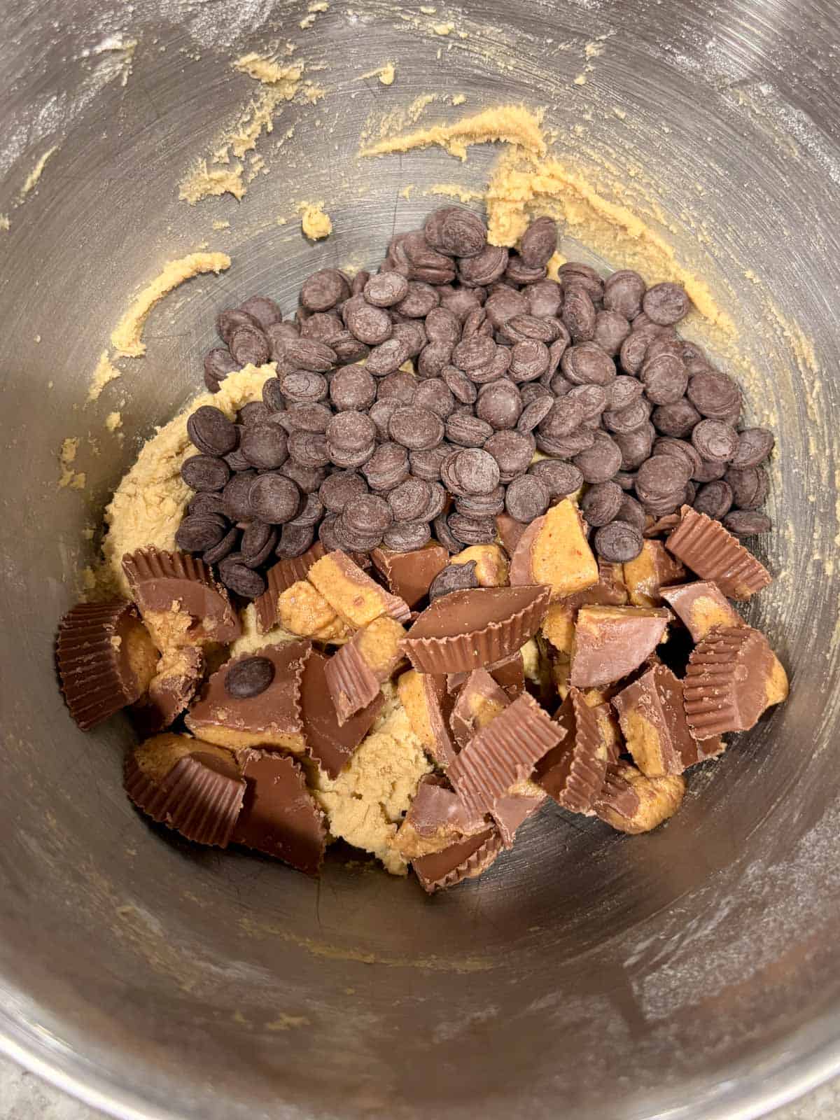 Peanut butter cups and chocolate chips being added to the cookie dough.