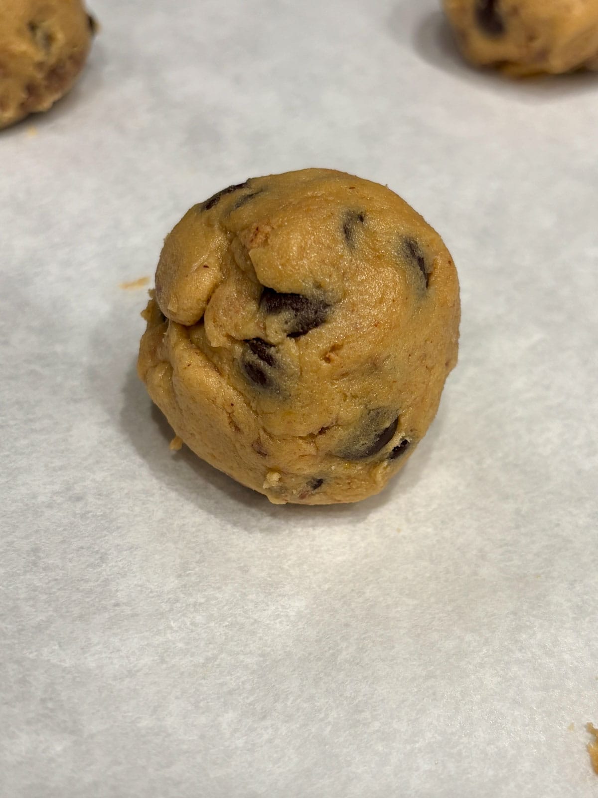 Cookie dough balls on a parchment lined baking sheet.
