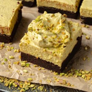 Pistachio brownies on cookie sheet with chopped pistachios and parchment paper.