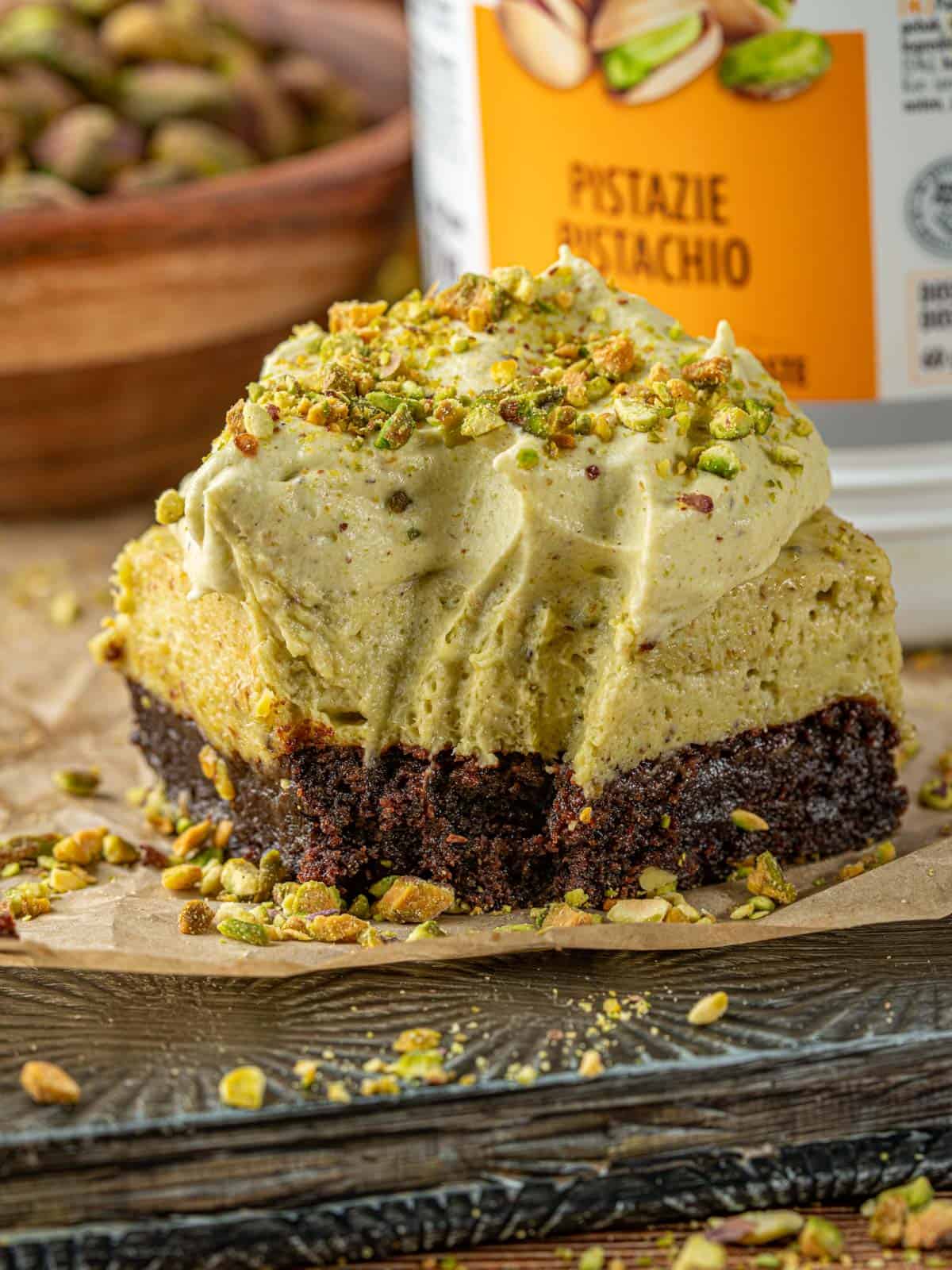 A pistachio brownie on a plate with pistachios around it.