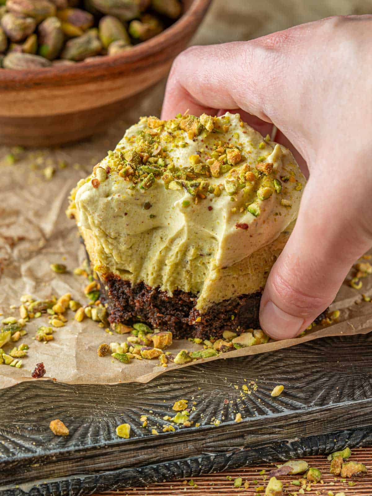 Brownies with a creamy pistachio cheesecake filling on top with chopped pistachios around.