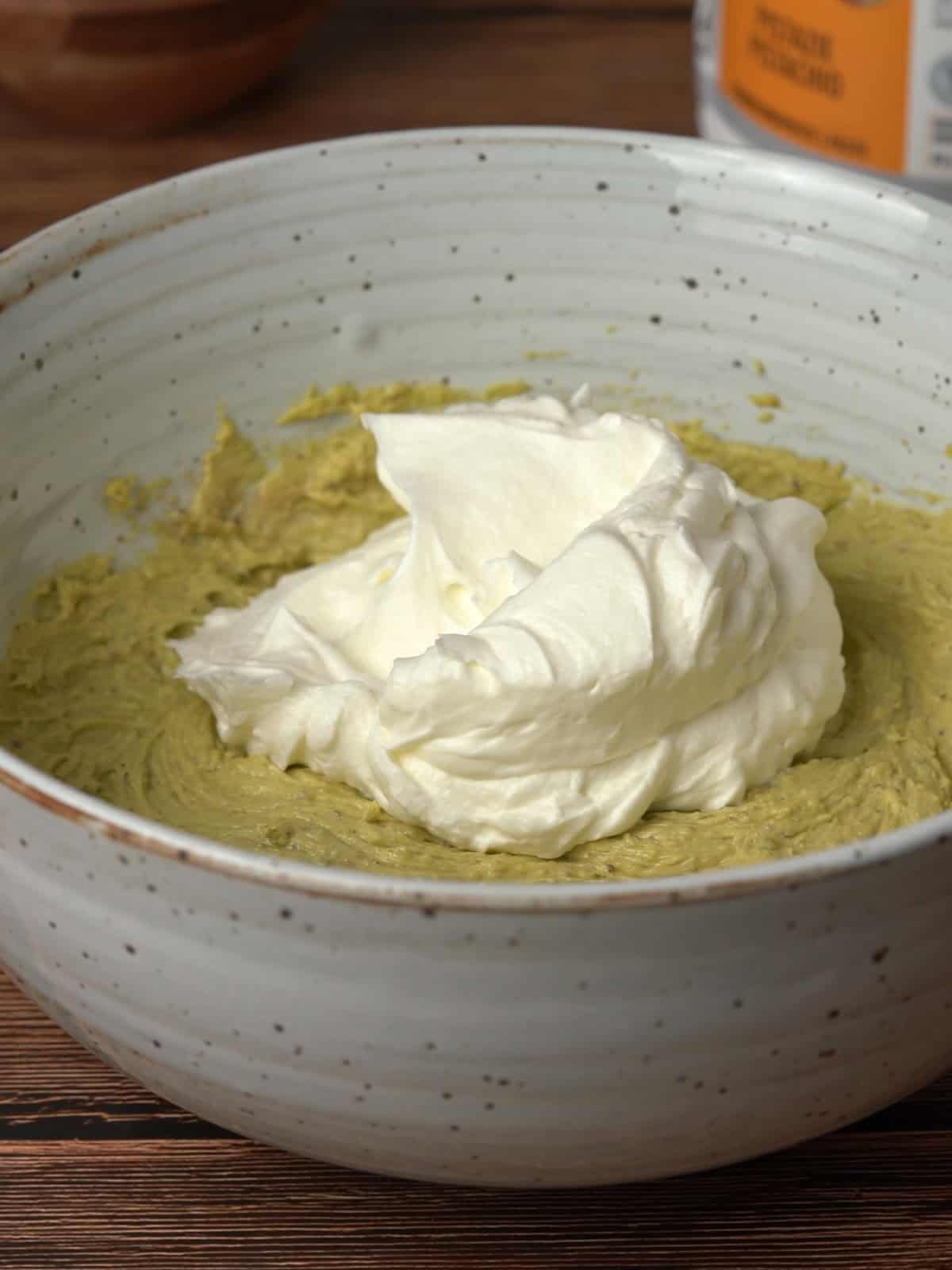 Whipped cream being added into the pistachio cream cheese mixture in a bowl.
