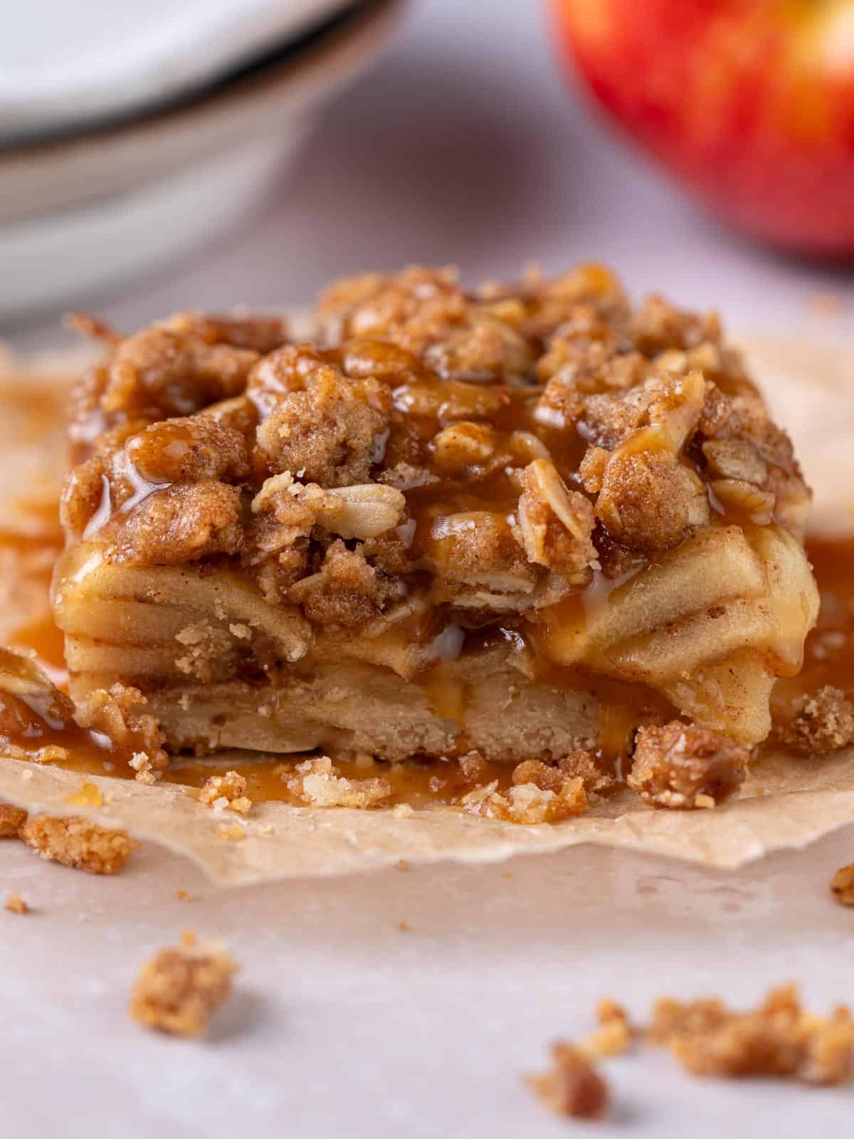 An apple pie bar with caramel on top and an apple in the background.