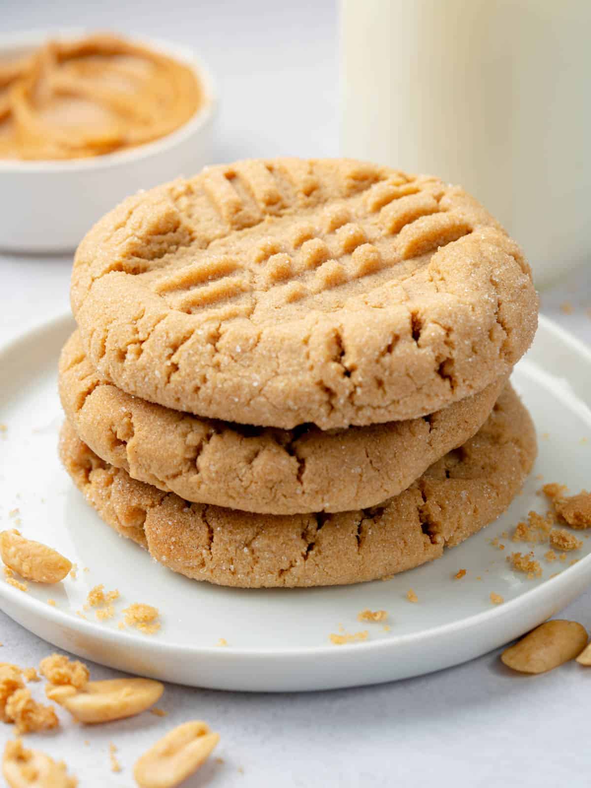 A stack of 3 cookies on top of each other on a plate with peanuts around.