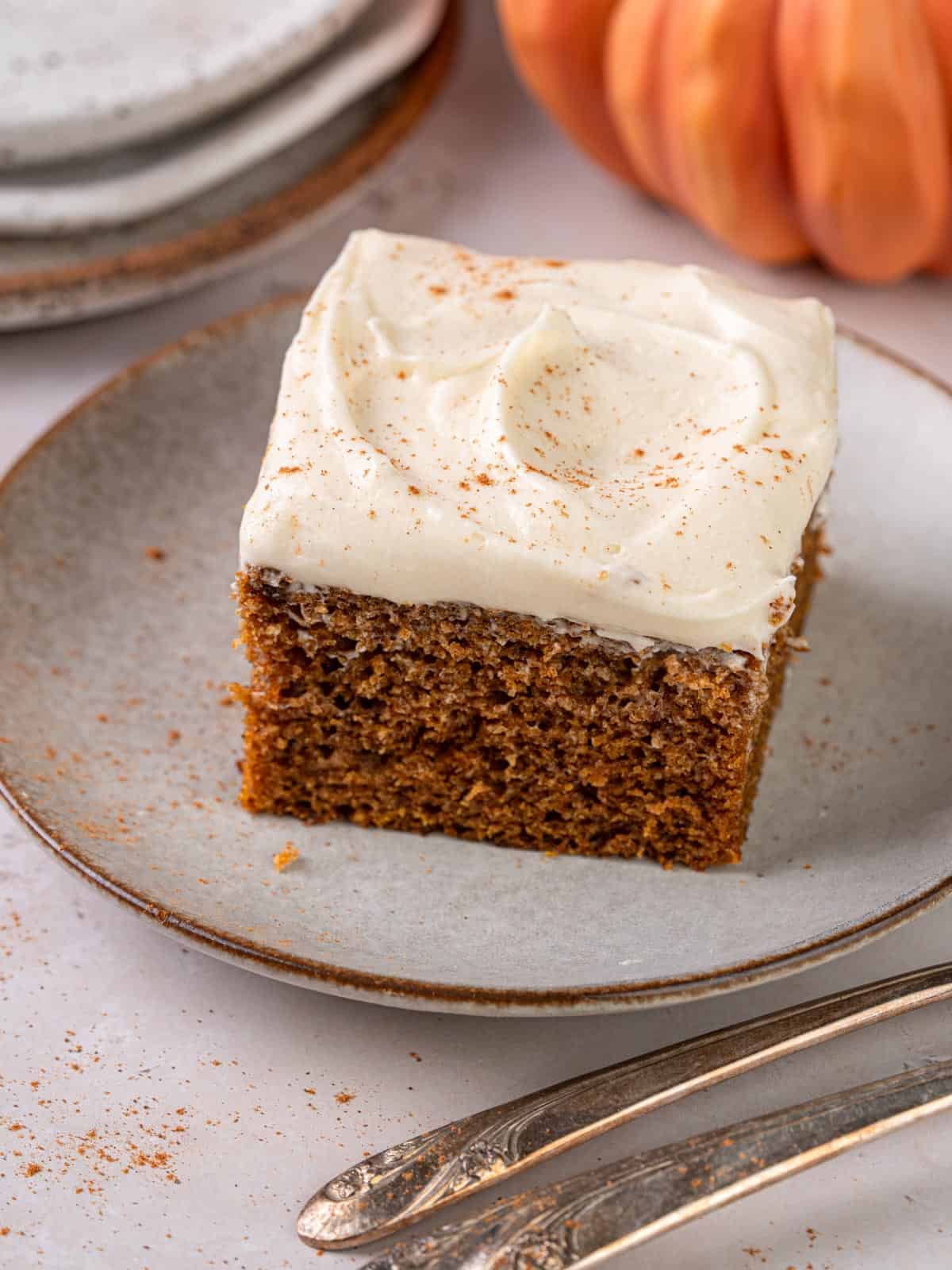 A slice of pumpkin cake made with olive oil on a plate with cream cheese frosting.