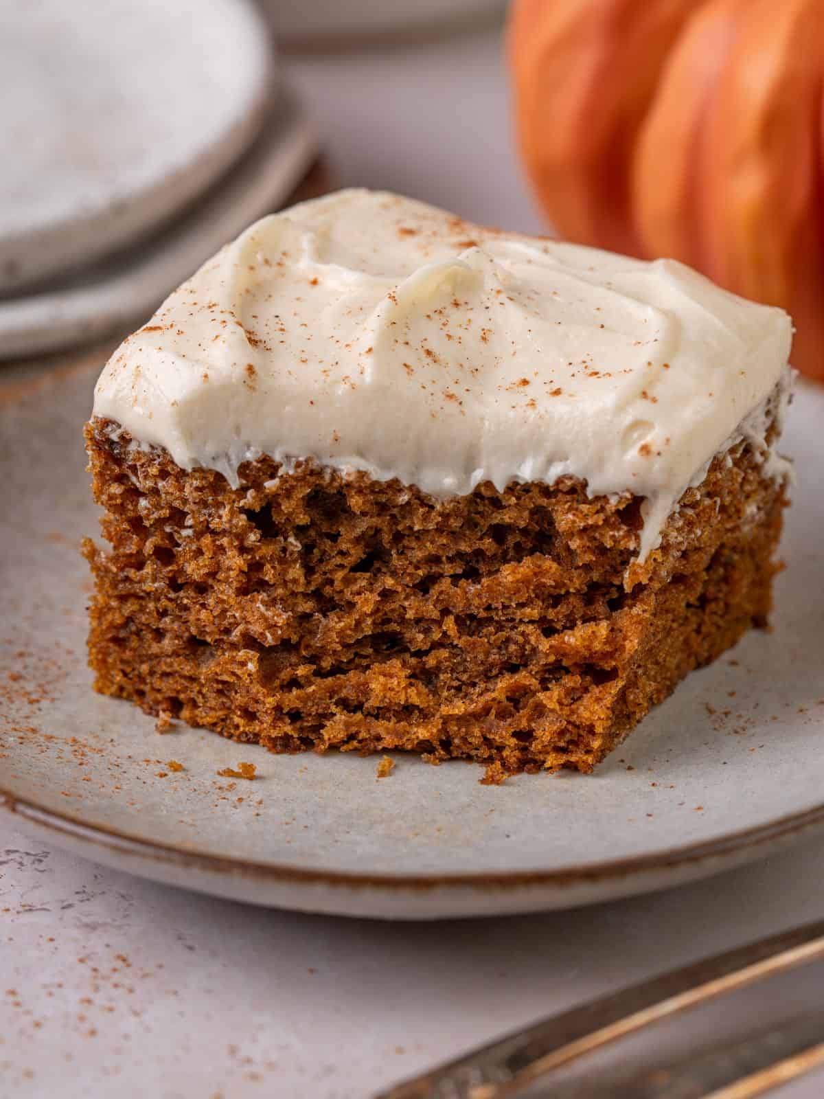 A slice of pumpkin cake made with olive oil on a plate with cream cheese frosting.