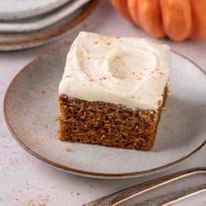 A slice of pumpkin cake made with olive oil on a plate with cream cheese frosting.