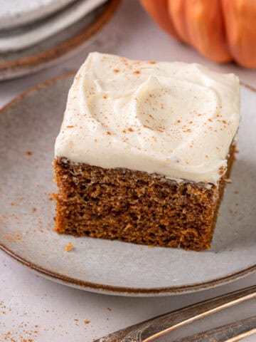 A slice of pumpkin cake made with olive oil on a plate with cream cheese frosting.