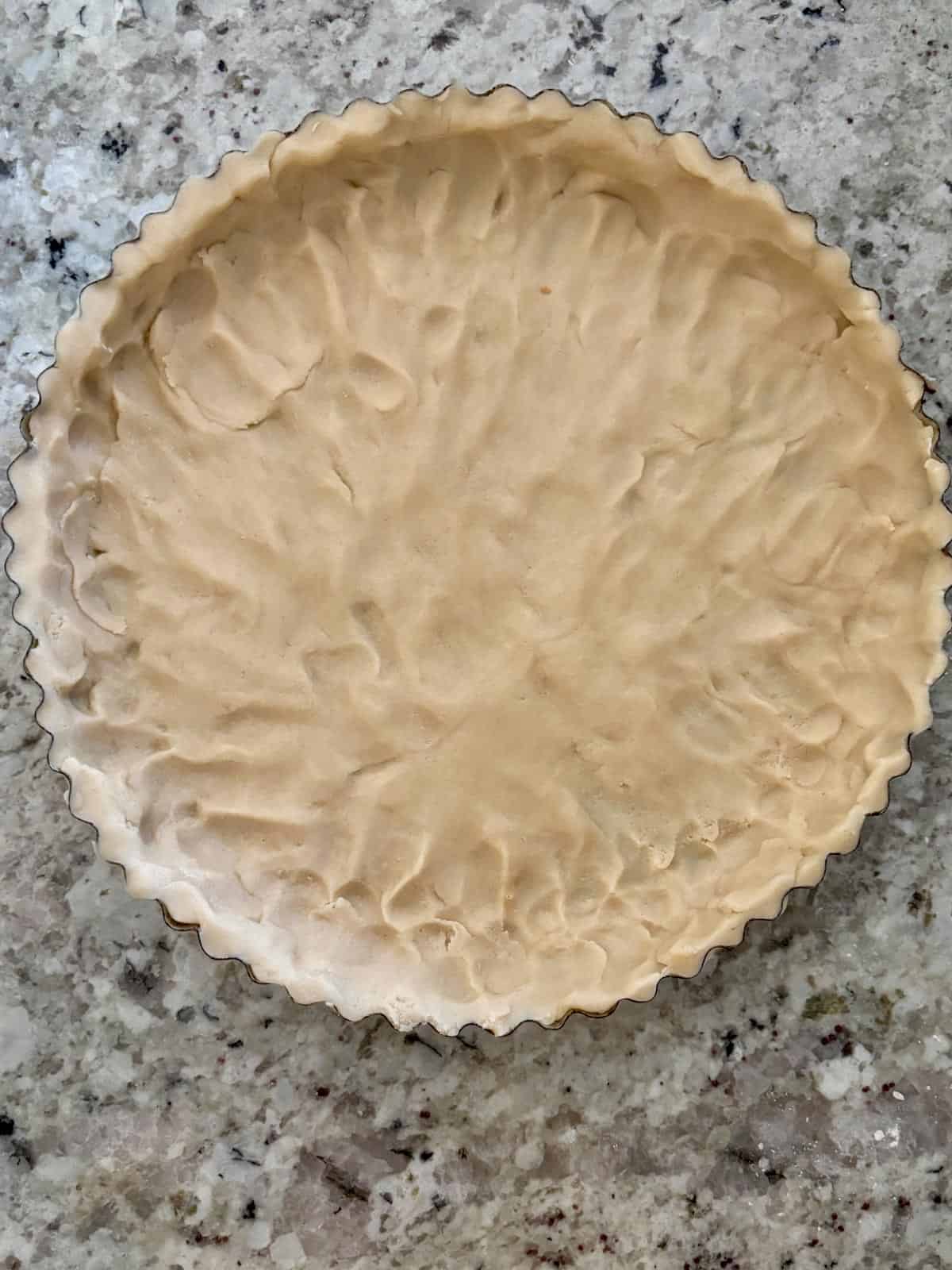 Tart dough being pressed into a 10 inch tart pan.