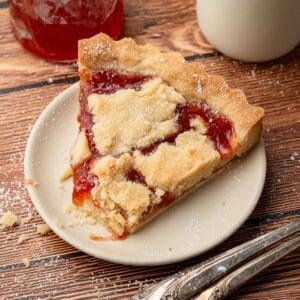 A piece of the strawberry jam tart on a plate with powdered sugar on top.